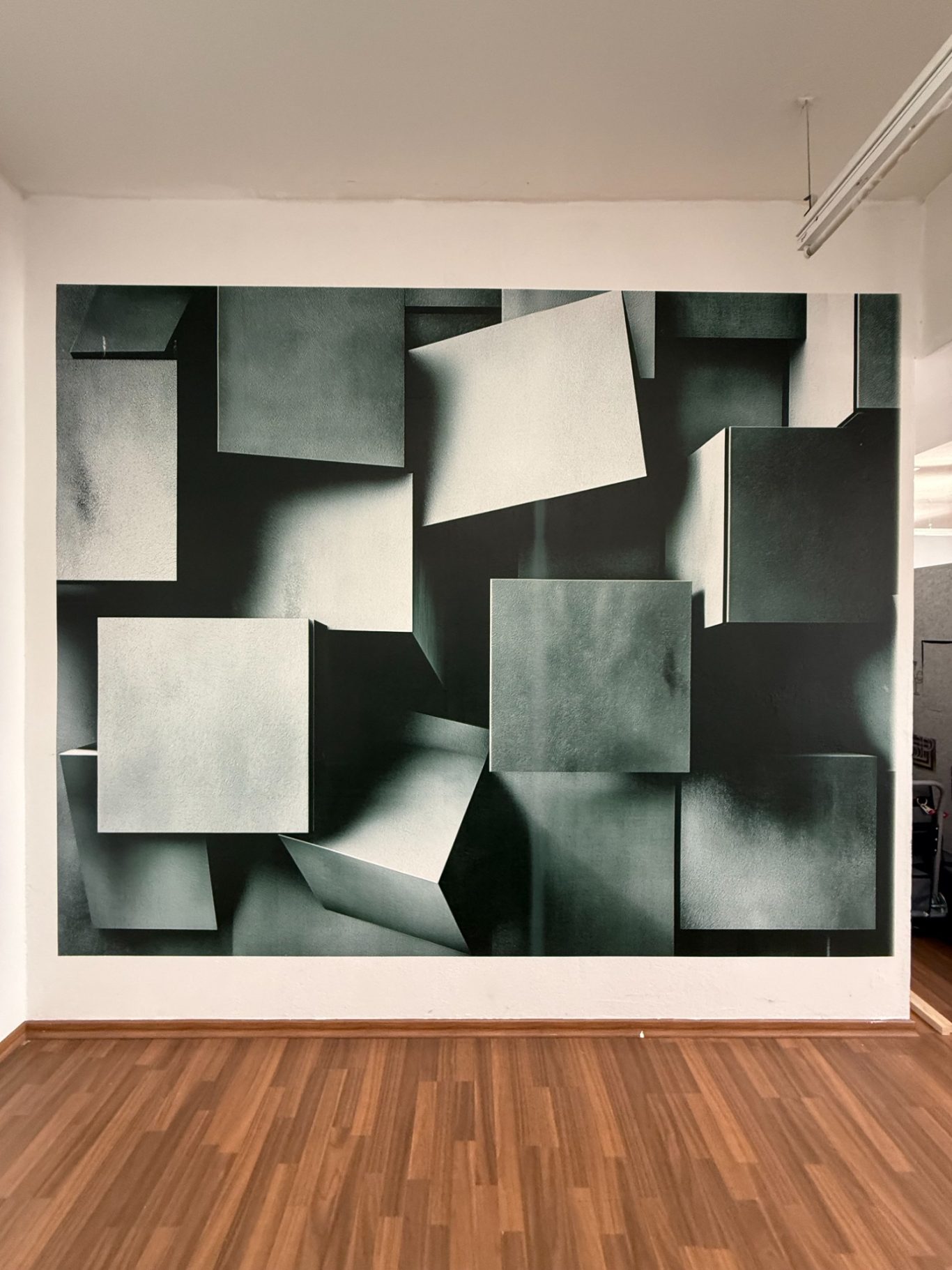 Abstrakte Wandgestaltung mit schwebenden, grau-schwarzen Würfeln und kubistischen Formen.